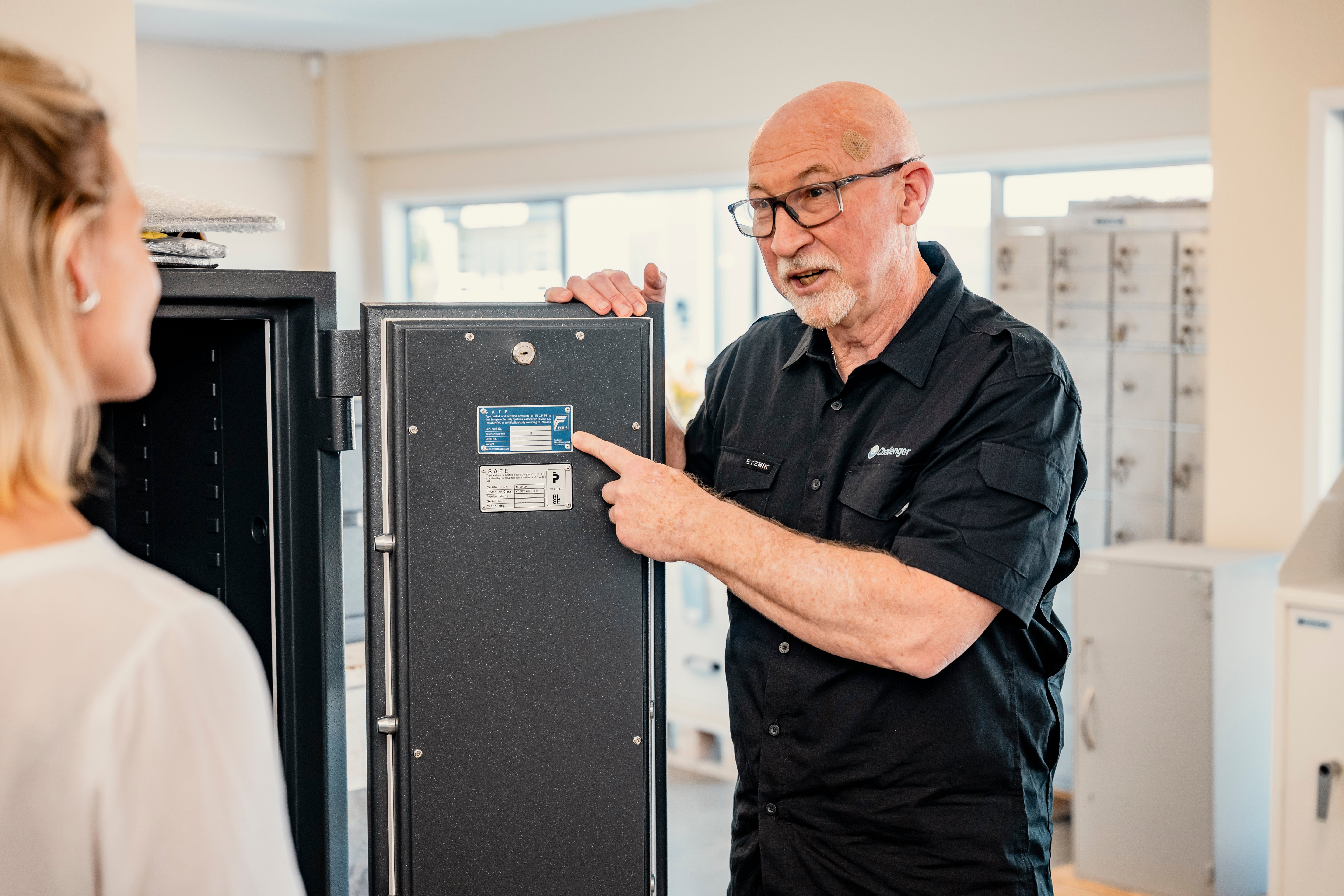 Man in a black shirt pointing at a refrigerator with a woman, likely in an appliance store.