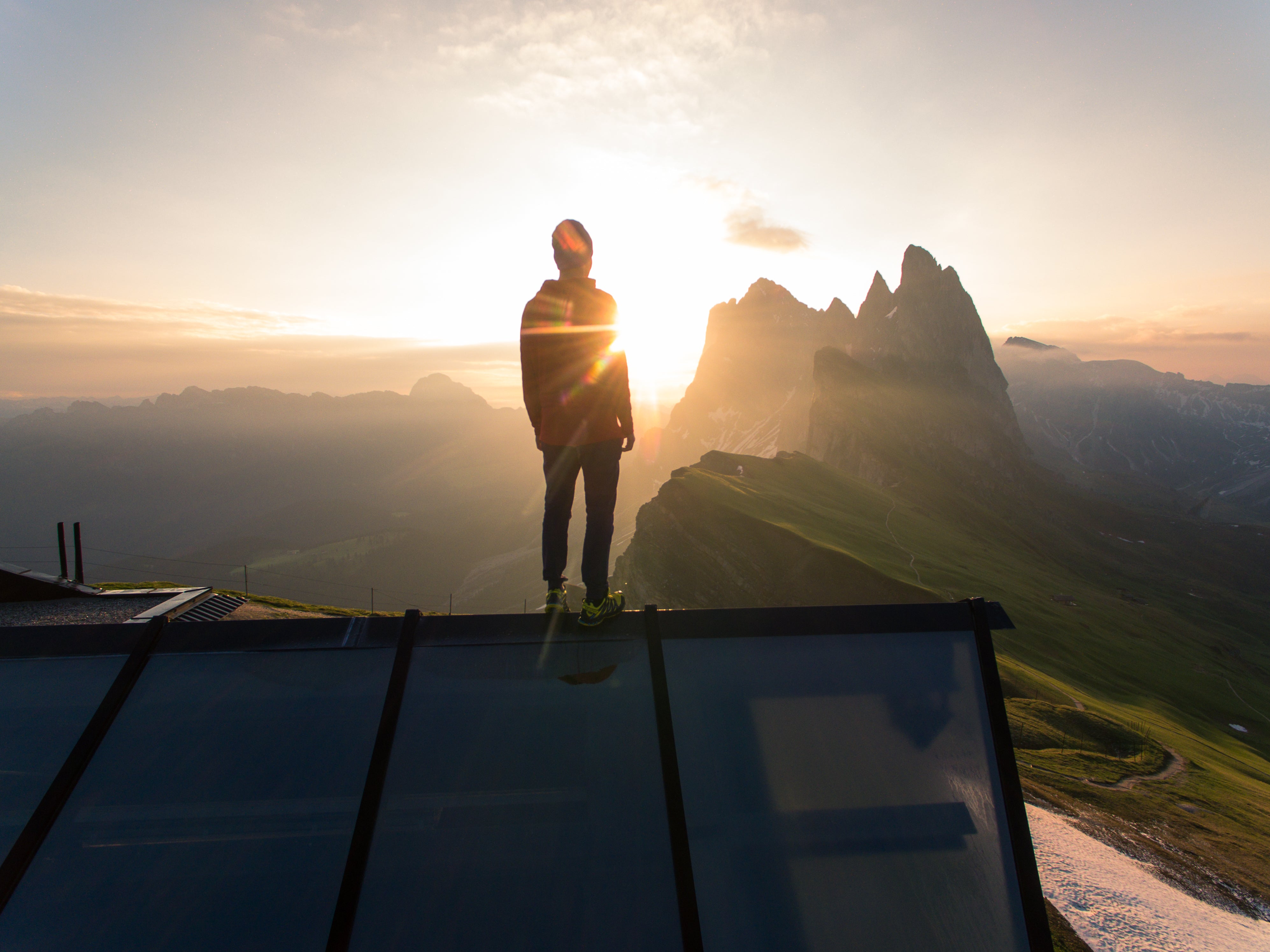 Man standing, looking out at sunrise from mountain top 